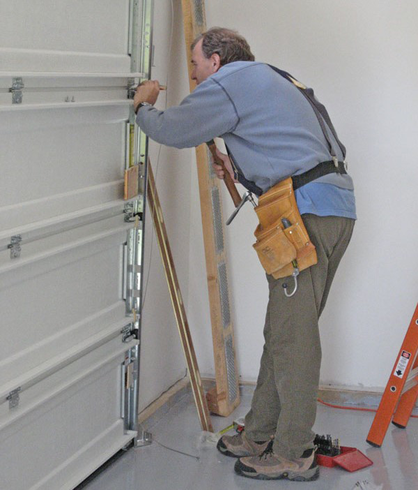 Technician performing precise installation and adjustments on a garage door to ensure durability and smooth operation, with ongoing maintenance services for optimal performance.
